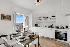 Una cocina moderna con armarios blancos, una mesa de comedor dispuesta con platos y vasos, y vistas a través de un ventanal abierto.