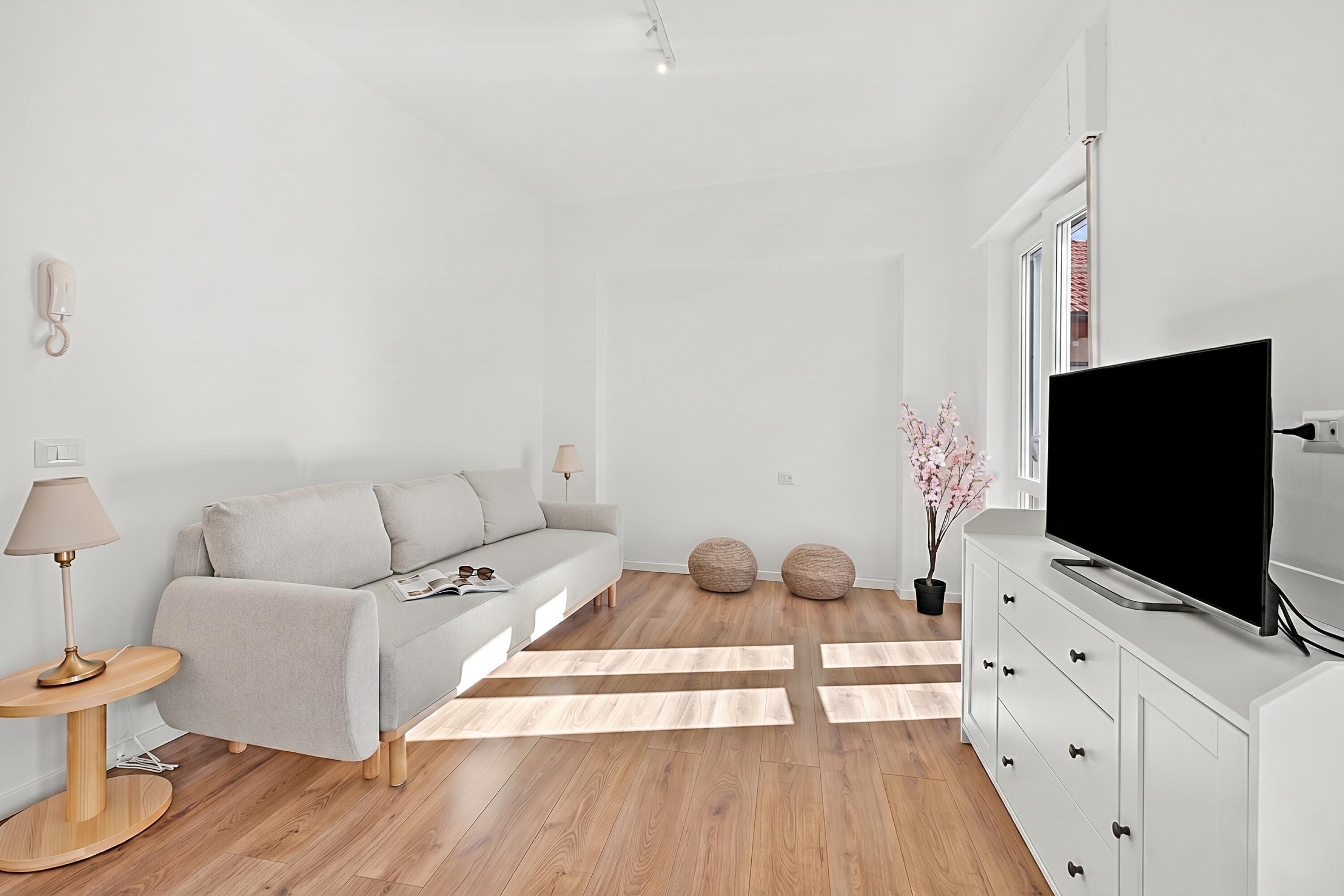 A modern living room with a sofa, a TV, a lamp, and a wooden floor.