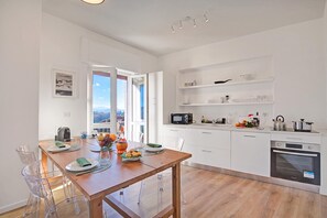 Eine moderne Küche mit weißen Schränken, einem Holztisch und Blick ins Freie durch ein großes Fenster.