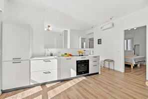Egy modern konyha fehér szekrényekkel, beépített sütővel és egy kis, kerek asztallal berendezett étkezővel.