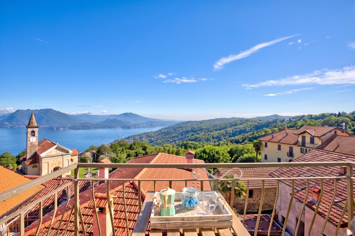 A terrace with a table, a view of a lake, mountains, and a church.