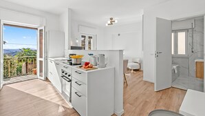 A modern kitchen with a central island, a dining area, and a bathroom with a marble wall. - Luce Lake View on Stresa Hill (Stresa)