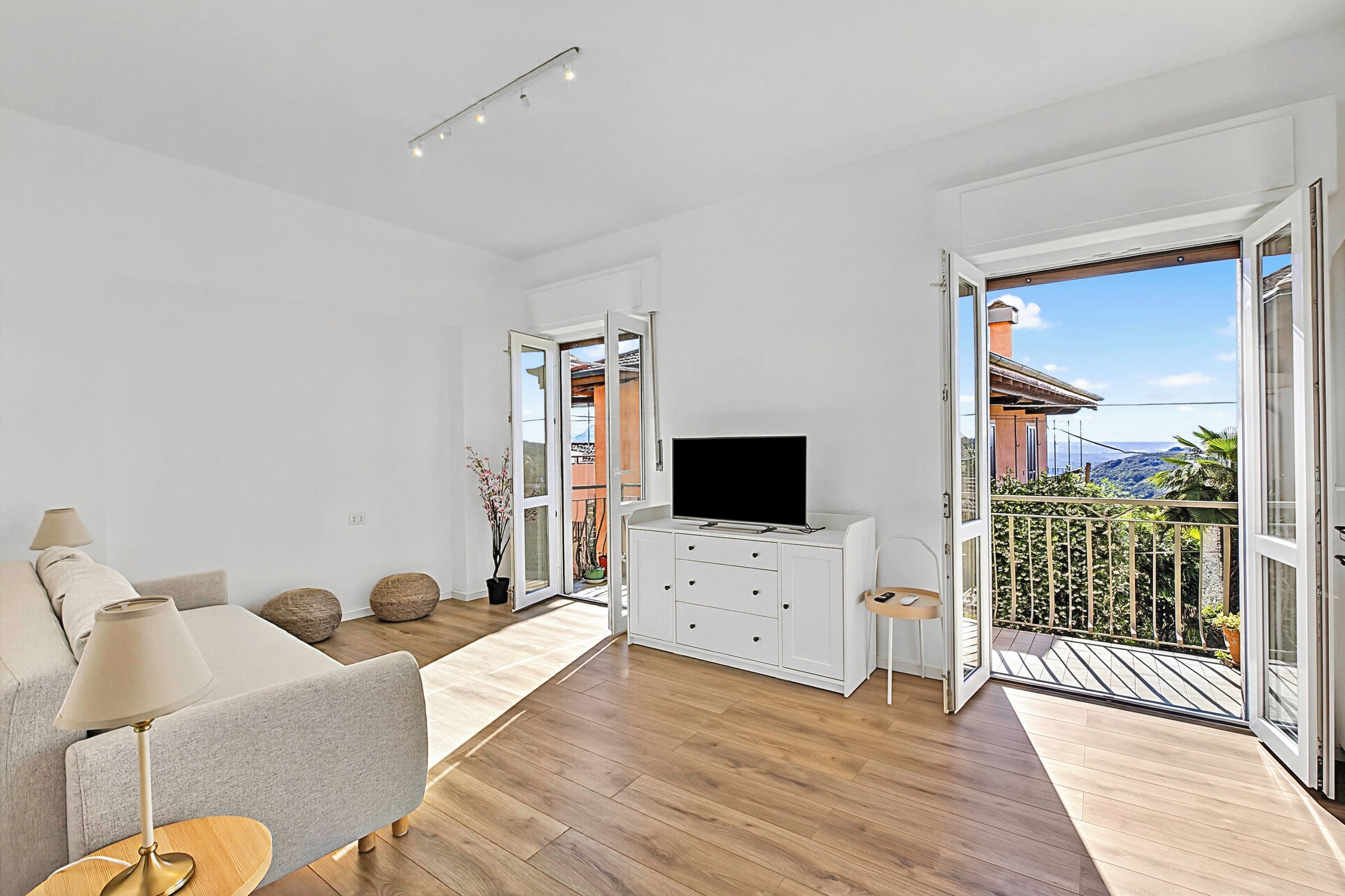 A modern living room with a sofa, TV, and a balcony with a view.