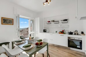 A modern kitchen with white cabinets, a dining table set with plates and glasses, and a view through an open window.