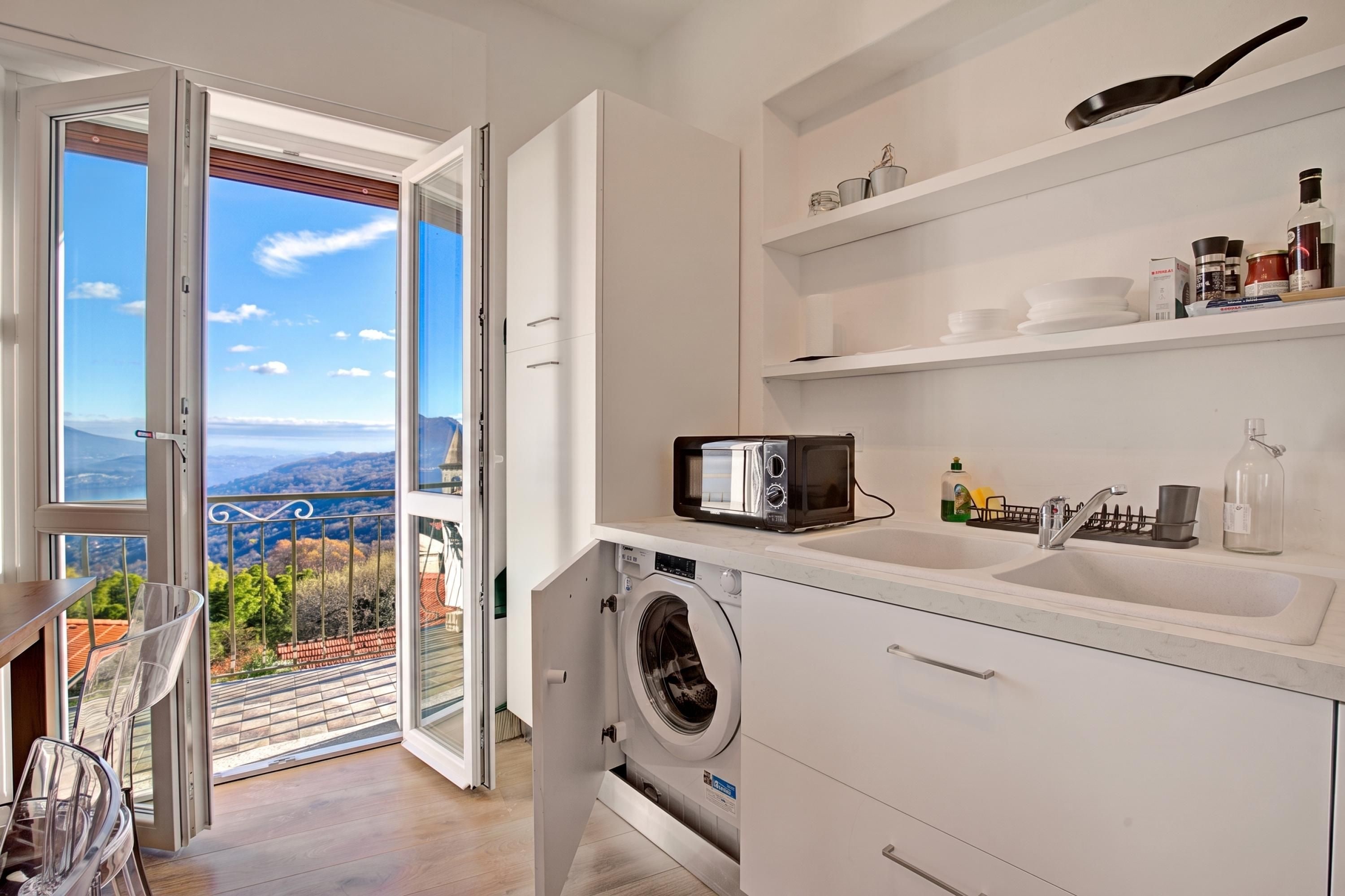 A modern kitchen with a built-in washing machine, a microwave, and a view of the outdoors.