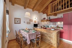 A wooden dining table with chairs, a kitchen island with pink cabinets, and a wooden ceiling.