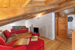 A cozy loft-style living room with a red sofa, wooden beams, a television, and a dartboard.