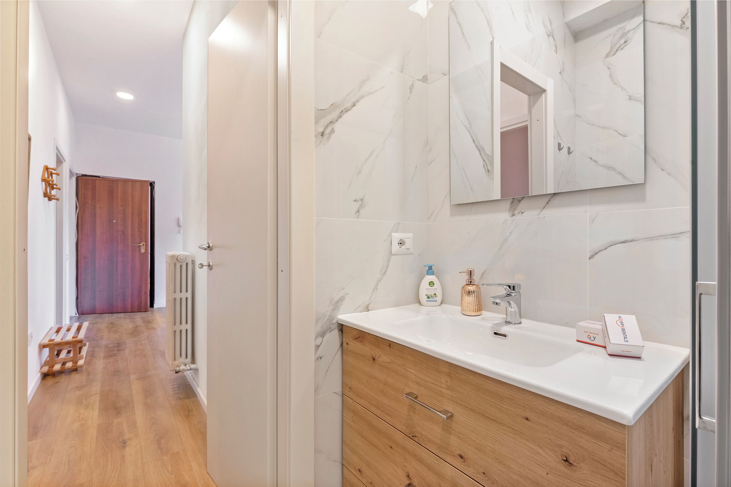 A modern bathroom with a marble backsplash, wooden vanity, and a large mirror.
