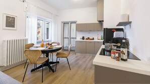 Egy modern konyha, étkezővel, melyben egy kerek asztal, nádfonatos székek, beépített tűzhely és egy kávéfőző található.