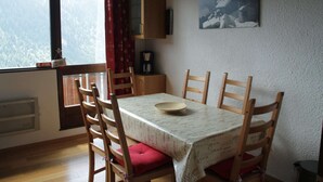 A dining area with a table, chairs, a cabinet, a coffee maker, and a view of a forest through a window.