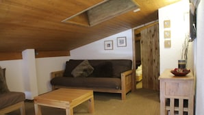 A cozy living room with a wooden ceiling, a sofa, a coffee table, and a small wooden cabinet with a bowl on top.