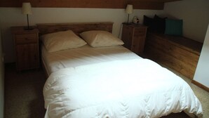 A bedroom with a wooden headboard, two bedside tables with lamps, a bed with white bedding, and a nightstand with a clock.