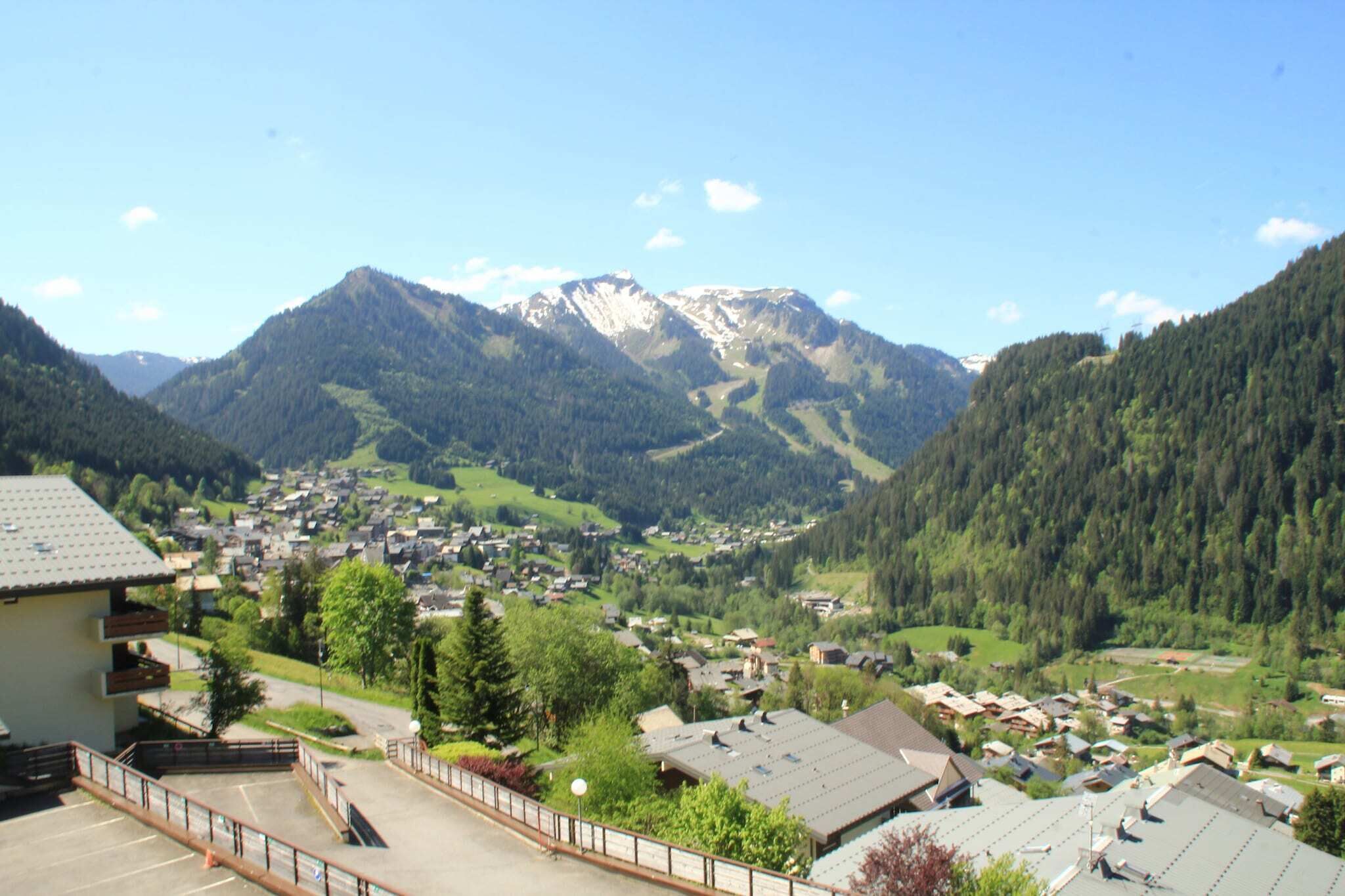 A mountain village with a view of snow-capped peaks, surrounded by lush greenery and residential buildings.