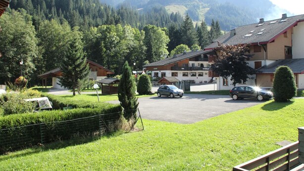 Un hotel con estacionamiento, rodeado de exuberante vegetación y montañas al fondo.