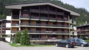 Un edificio de varios pisos con balcones, una señal que indica que es un hotel y coches estacionados adelante.