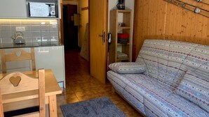 Kompakti oleskelutila, jossa on pieni keittiönurkkaus, sohva ja puinen kaappi.