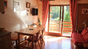 A dining area with a wooden table and chairs, a sofa, and a sliding glass door leading to an outdoor deck. - Apartment in Chatel in ski resort (Châtel)