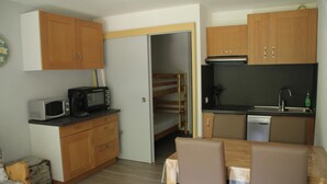 A compact kitchen with wooden cabinets, a microwave, a sink, and a dining table with chairs. - Apartment in Portes du Soleil (Châtel)