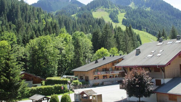 A lodge with a large building, a parking area, and a view of a forested mountain range. - Apartment in Portes du Soleil (Châtel)