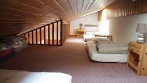 Ein gemütliches Schlafzimmer im Dachgeschoss mit geneigter Decke, einem Einzelbett, einem Nachttisch und einem kleinen Tisch mit Lampe.