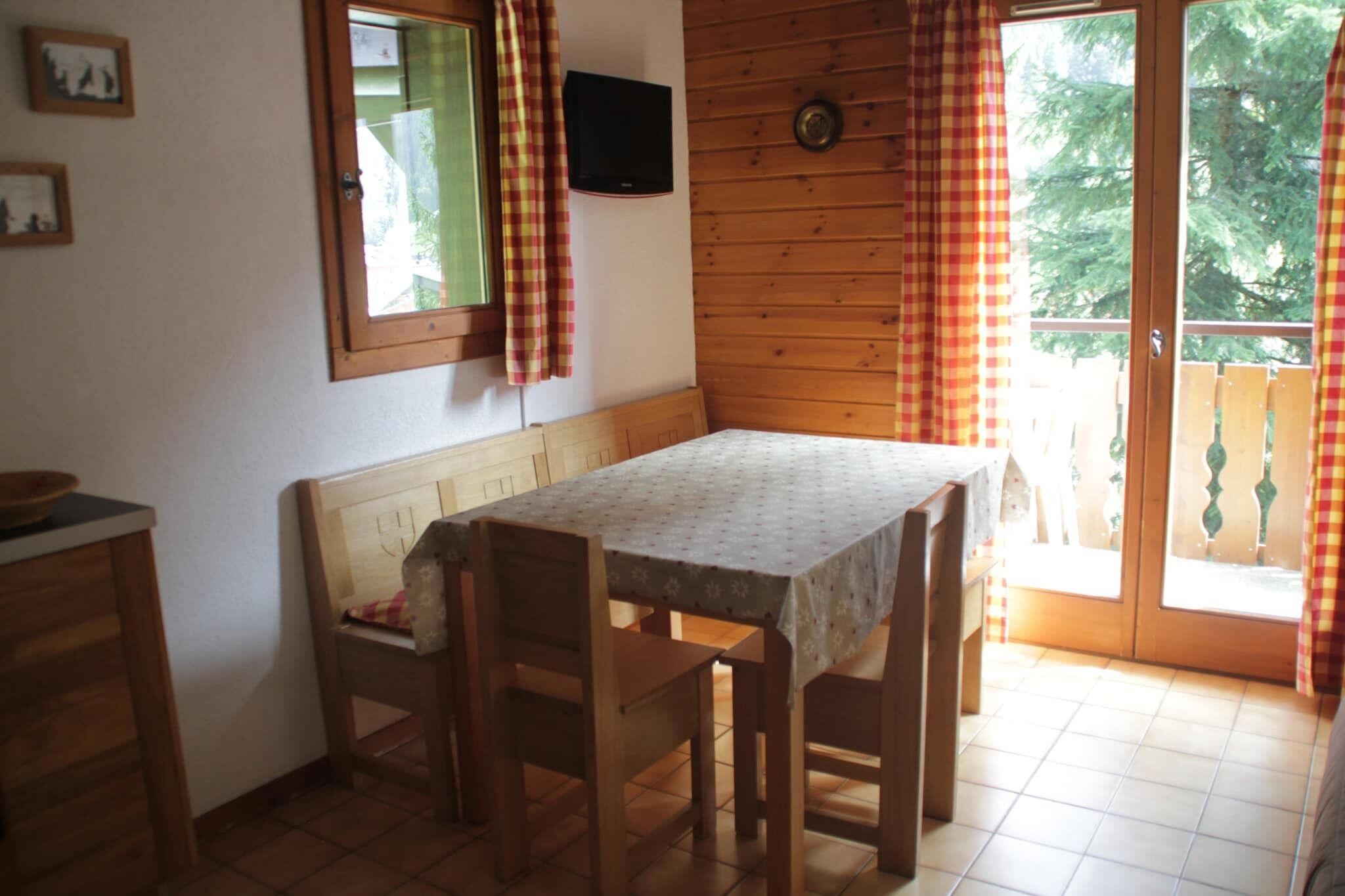 A cozy room with a wooden bench and table, a window with curtains, and a door leading outside.