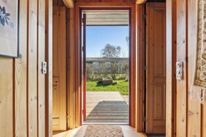 Ein Holzinnenraum, der zu einer Holzdielenterrasse mit Blick auf einen Garten und ein Gebäude in der Ferne führt.