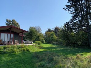 A building with a red roof and a covered porch with chairs. - Cozy cottage with a beautiful view (Tranekær)