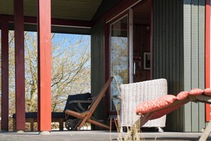 Une véranda couverte avec une chaise en bois, une chaise en osier et un banc.