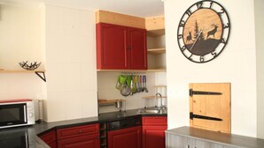Una cocina con armarios rojos, un microondas, un lavamanos y una puerta de madera.