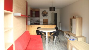 Un espacio habitable compacto con kitchenette, una zona de comedor con mesa redonda y sillas, un sofá rojo y un mueble de madera.