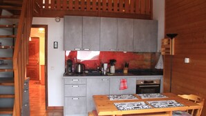 Une cuisine avec des meubles de couleur grise, une table en bois recouverte d’une nappe à carreaux rouges et blancs, et un banc en bois.