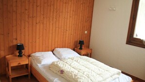 Une chambre aux murs lambrissés, avec un lit simple, deux tables de chevet dotées de lampes et une fenêtre sur le mur de droite.