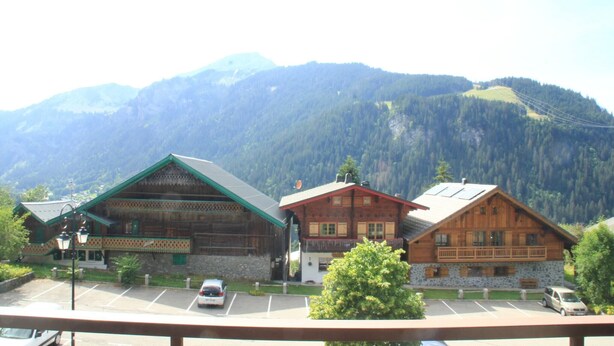 Un chalet de montagne composé d’un grand bâtiment en bois, d’une annexe plus petite attenante et d’un parking.
