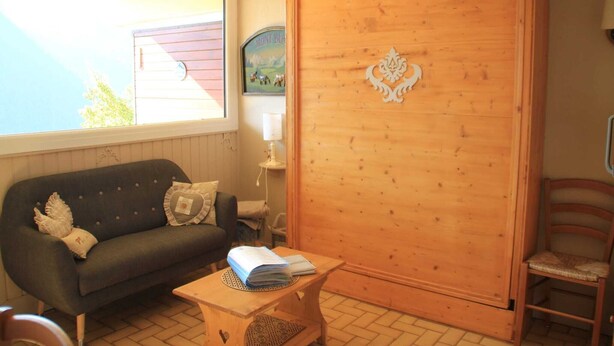 A cozy room with a dark green sofa, a wooden table with a book, and a wooden door with a decorative emblem. - Apartment in Châtel near Cable Car (Châtel)