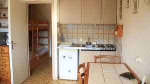 A compact kitchen with a refrigerator, stove, and sink. There is a wooden bunk bed in the adjacent room. - Apartment in Châtel near Cable Car (Châtel)