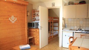 A compact kitchen with a microwave, refrigerator, and wooden cabinets. A bunk bed is visible in the background. - Apartment in Châtel near Cable Car (Châtel)