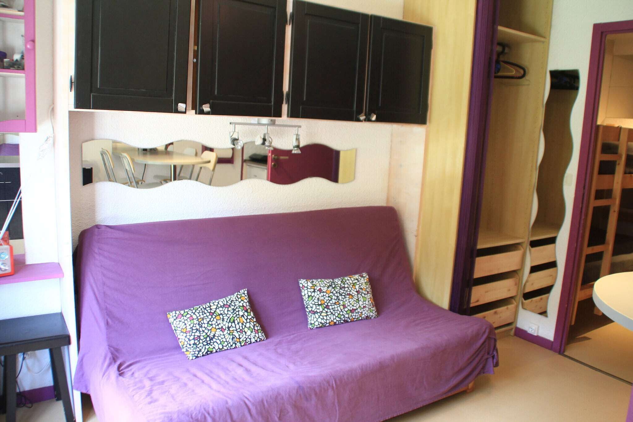 Ein violettes Sofa mit gemusterten Kissen, ein kleiner Tisch und ein Spiegel darüber.