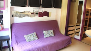 A purple sofa with patterned cushions, a small table, and a mirror above it.