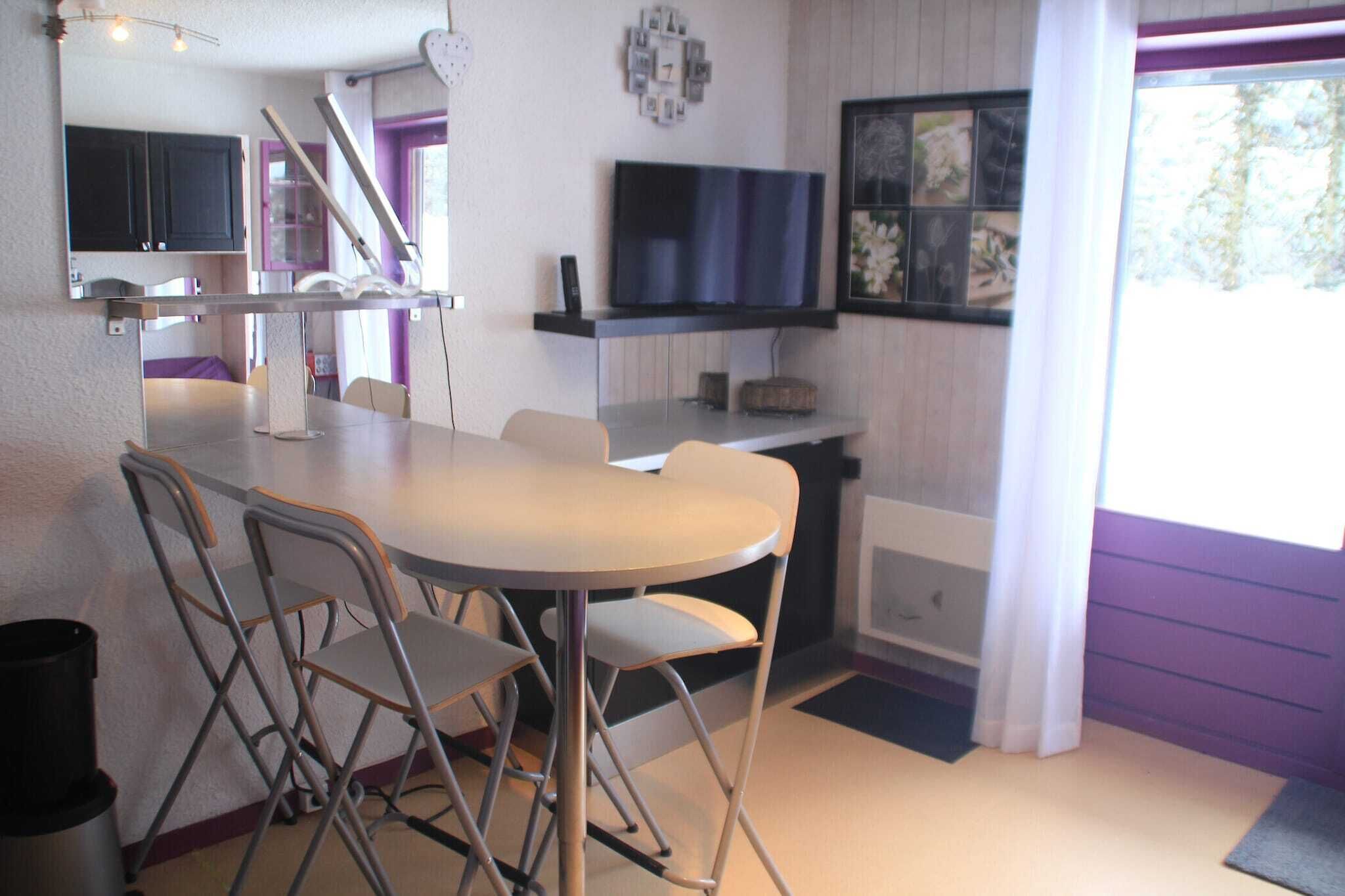 A compact kitchen with a dining area, a TV mounted on the wall, and a window with curtains.