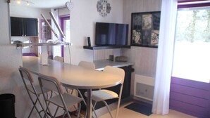 A compact kitchen with a dining area, a TV mounted on the wall, and a window with curtains.