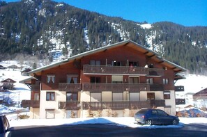 A multi-story building with balconies, a car parked in front, and a mountainous backdrop. - Apartment in Chatel for 4 people (Châtel)