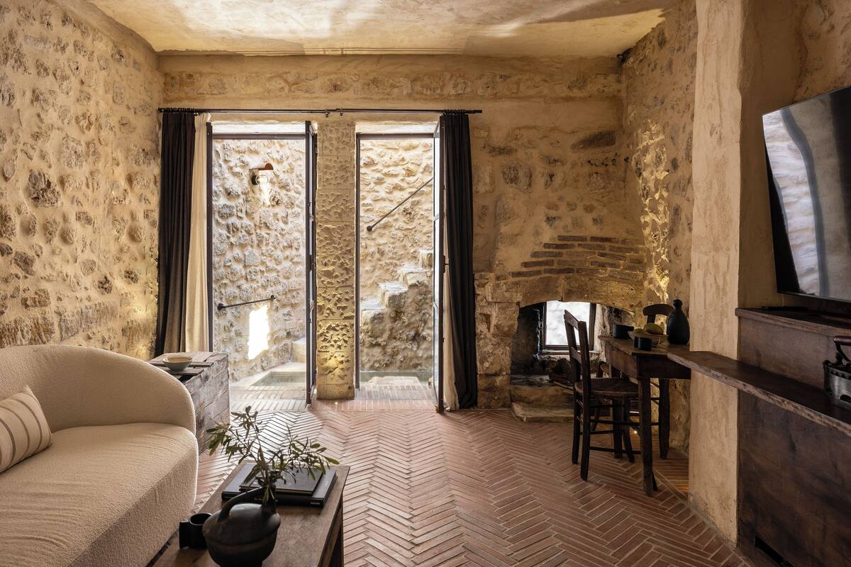Una habitación rústica con paredes de piedra, suelo de espiga, un sofá, una mesa de comedor y una chimenea.