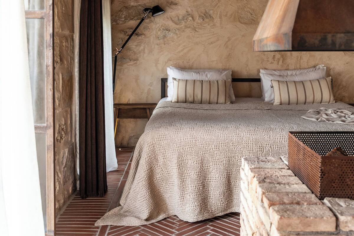 Un dormitorio rústico con piso de ladrillo, techo de madera y cama con almohadones a rayas.
