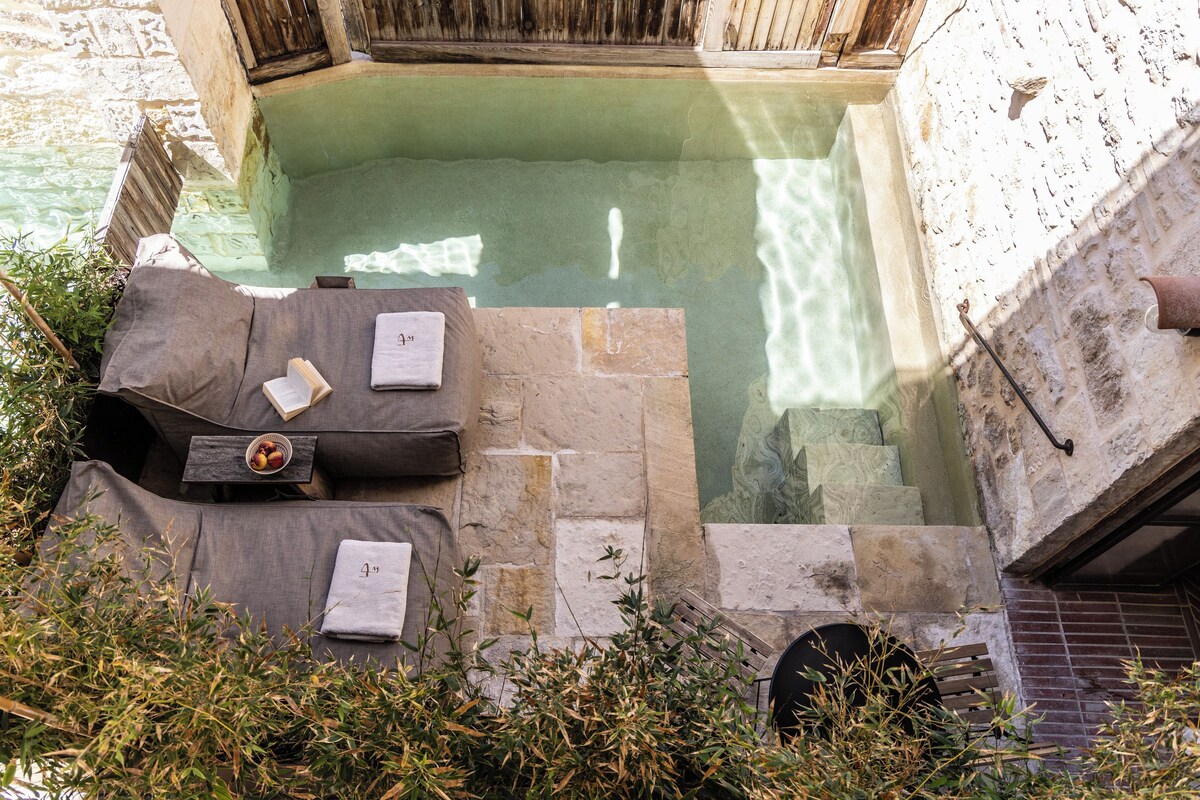 Una piscina de piedra con cubierta de madera, un banco y una pequeña mesa con un libro y un cuenco de fruta.