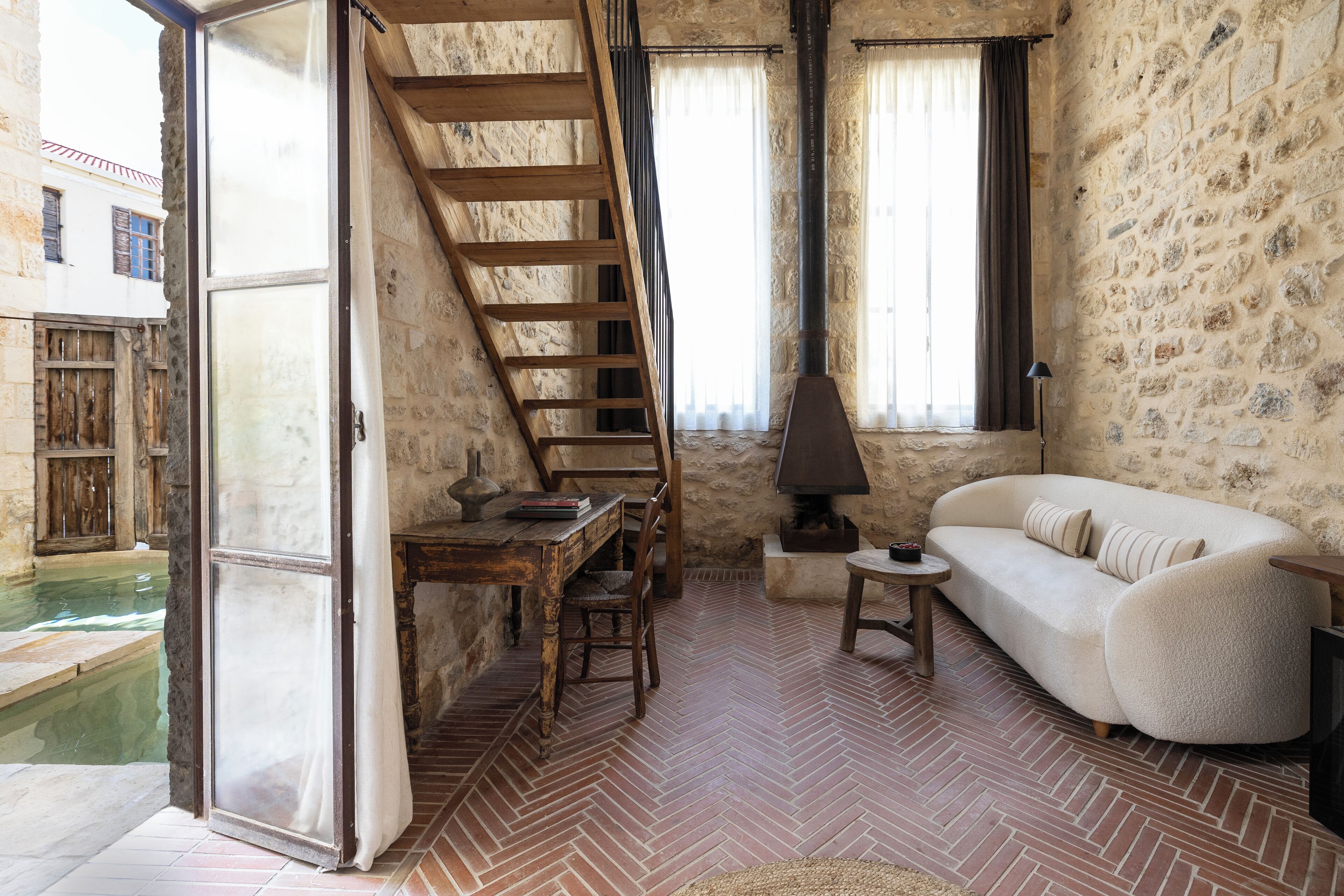 A rustic room with a herringbone floor, a wooden ladder, a white sofa, and a stone wall.