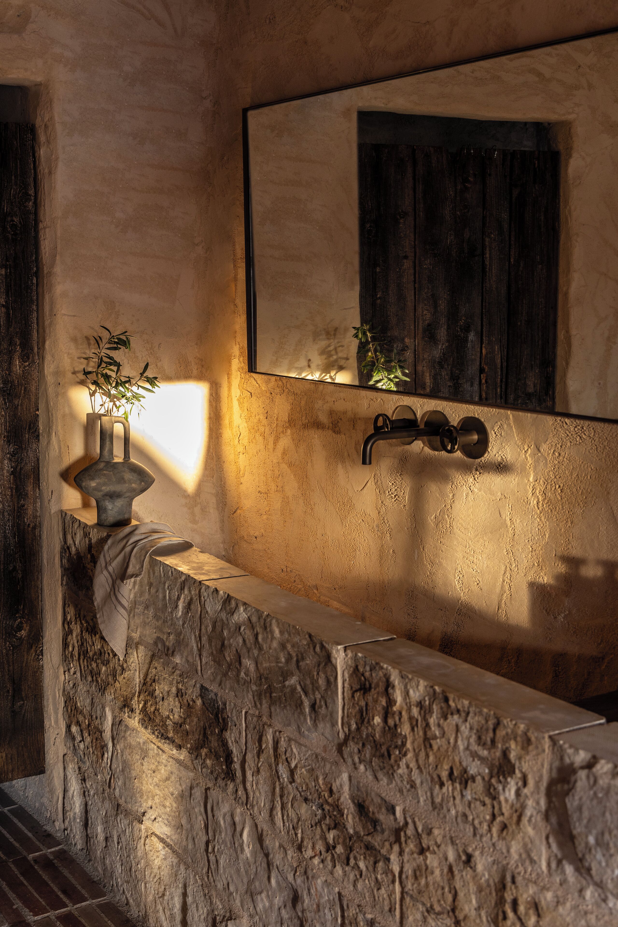 A stone bathtub with a wooden door, a potted plant, and a mirror above it.