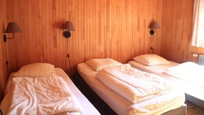 A room with wooden walls, two beds with white bedding, and two wall-mounted lamps.