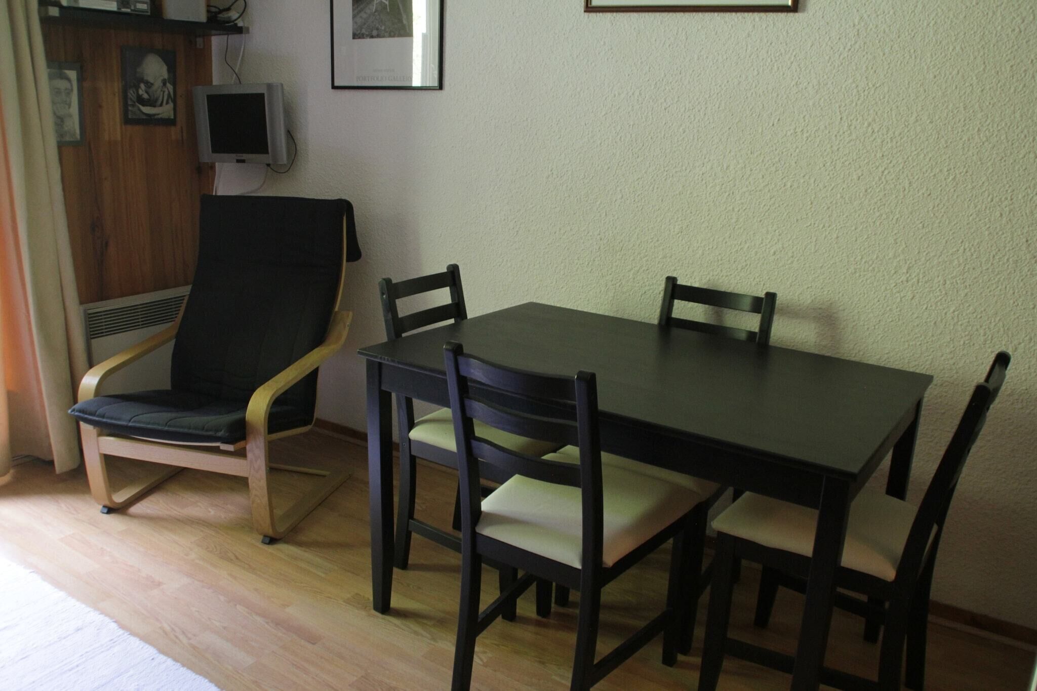 Ein Essbereich mit einem Tisch, vier Stühlen, einem Fernseher an der Wand und einem gerahmten Bild über dem Tisch.