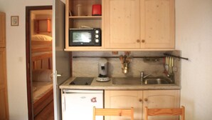 Eine kleine Küche mit Mikrowelle, Kaffeemaschine und Spüle. Im angrenzenden Raum ist ein Etagenbett zu sehen.