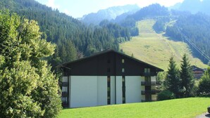 Ein zweistöckiges Gebäude mit schrägem Dach, einem Balkon im oberen Stockwerk und Blick auf eine gebirgige Landschaft.